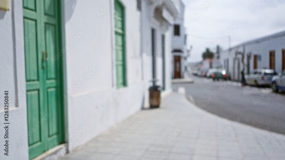 Blurred street view in lanzarote, spain with green door and white buildings, displaying a defocused outdoor scene with parked cars and people in the background. Blurred street view in lanzarote, spain with green door and white buildings, displaying a defocused outdoor scene with parked cars and people in the background.