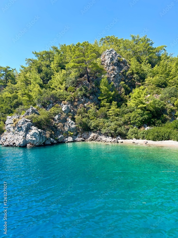 The crystal clear blue waters of the Mediterranean Sea against the mountains and trees The crystal clear blue waters of the Mediterranean Sea against the mountains and trees