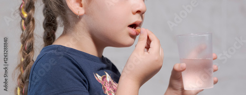 5-year-old girl taking a medicine pill with a glass of water, concept of self-medicating photo