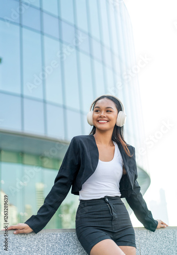 Free Download Young Asian Businesswoman Listening to Music with Headphones Outdoors in Modern Office District - GFXLoad