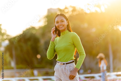 Young Asian Woman Talking on Phone Outdoors in a Park During Sunset