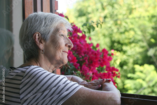 portrait of senior latino woman looking through the window at her garden 