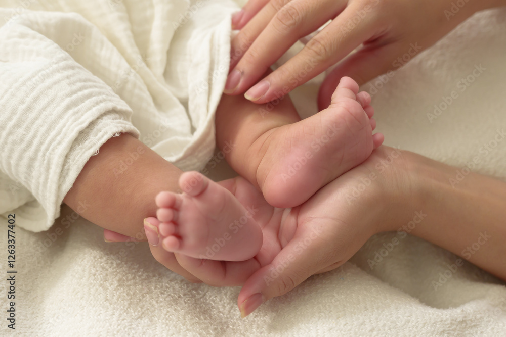 Asian newborn baby is lying on a bed. Tiny feet in mother’s hands. Gentle touch symbolizes deep love, care, and bonding. Soft skin and warmth create a serene and comforting moment of connection.