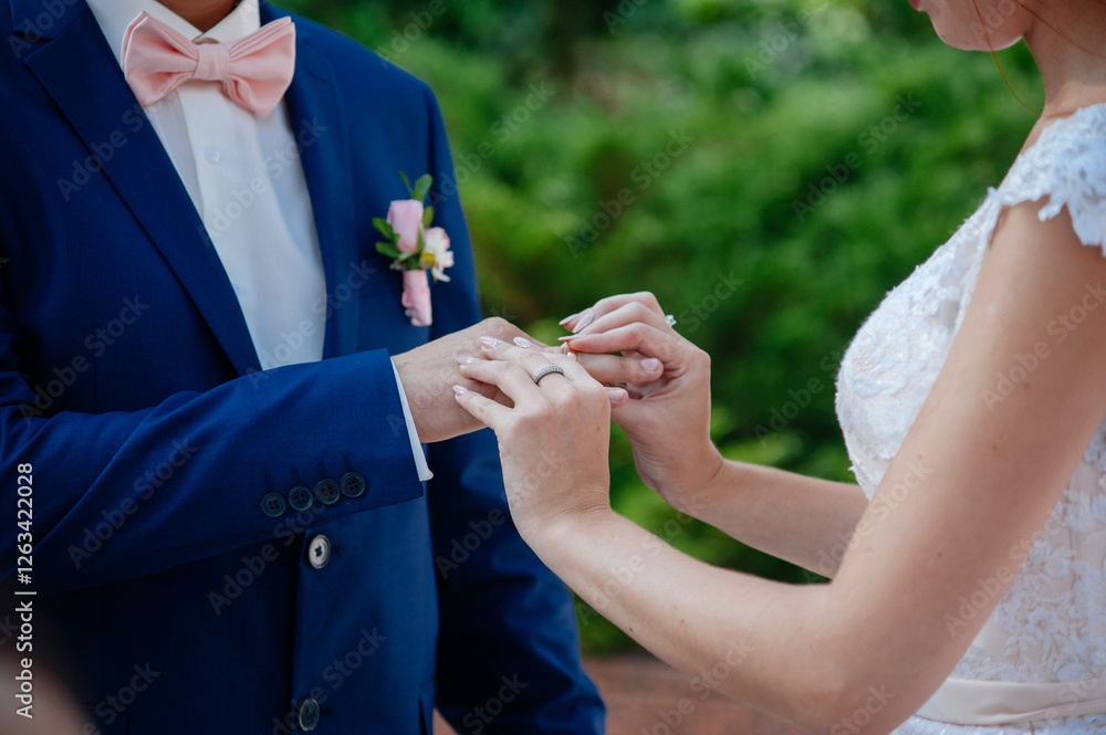 Fototapeta premium Close-up of the bride placing the wedding ring on the groom's finger during their wedding ceremony outdoors.