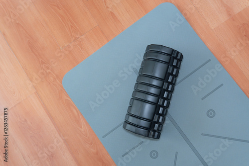 Sports equipment for home fitness. The massage roller helps stimulate lymphatic flow and relieve muscle tension after exercises. Black massage roller on a gray exercise mat with geometric patterns. photo