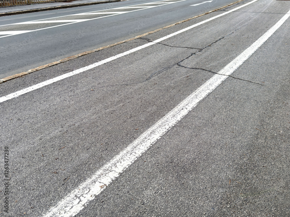 Urban road with cracks and faded white lines on asphalt surface Urban road with cracks and faded white lines on asphalt surface