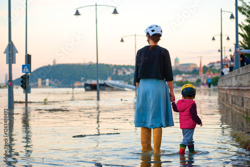 Mother and son hand in hand standing in the water and watching the flood in the city