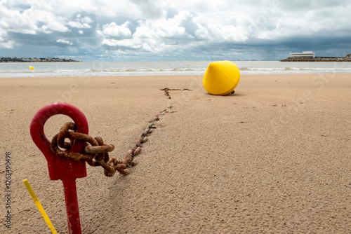 A sandy beach with a yellow boye and a long iron chain that evokes the desire to travel by boat