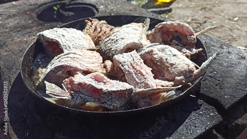 Fish is fried in frying pan close up. Cooking fresh fish catch. Successful fishing. Delicious fish dish fried over the fire. Dish from fried fish cooked on fire. Pleasant rest in nature