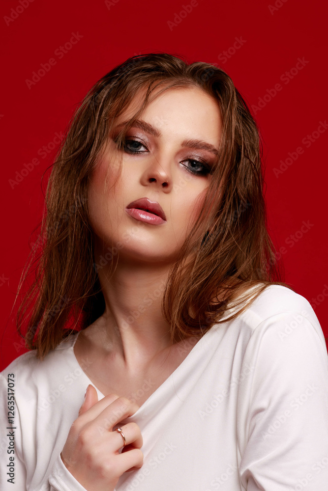 Girl with smokey eye makeup in a white silk dress, on a red background. Fashion pose.