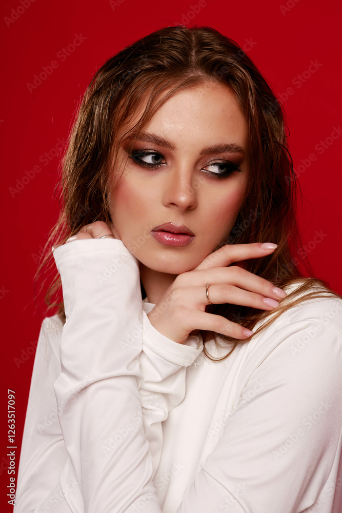 Girl with smokey eye makeup in a white silk dress, on a red background. Fashion pose.