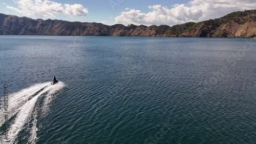 Vista panorámica de lago profundo entre montañas con lancha rápida dejando estela.