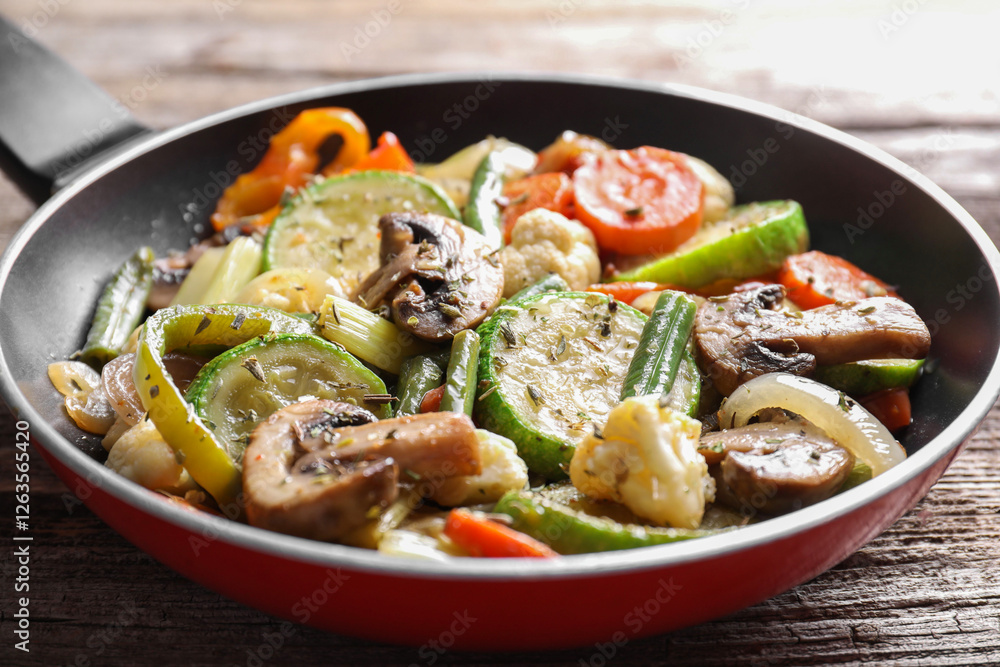 Different vegetables and mushrooms in frying pan on wooden table, closeup Different vegetables and mushrooms in frying pan on wooden table, closeup