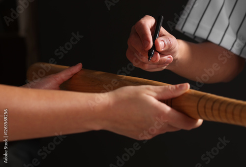Canvas Print Baseball player signing autograph on bat against black background, closeup