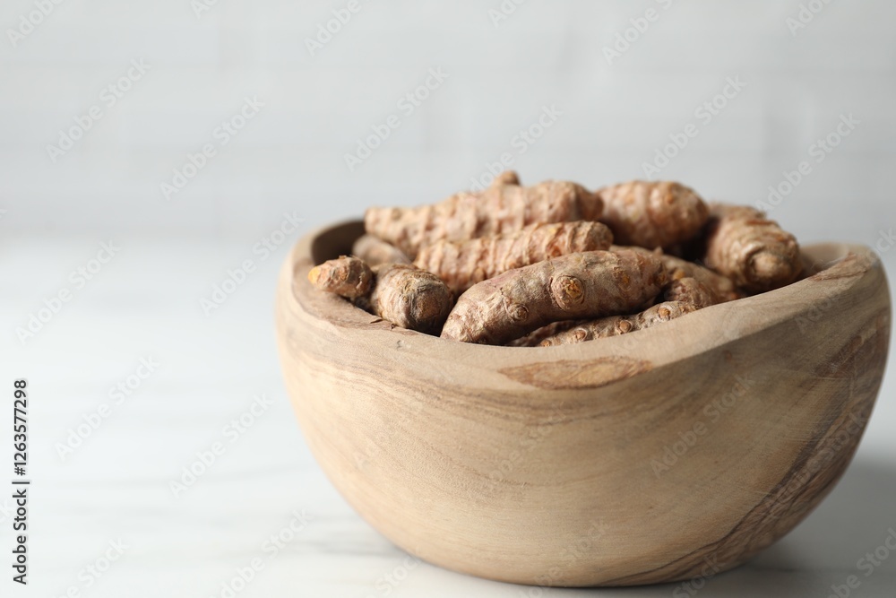 Raw turmeric roots in bowl on white table, closeup. Space for text Raw turmeric roots in bowl on white table, closeup. Space for text