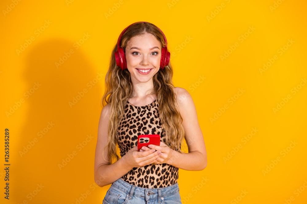 Young woman with leopard print top smiling while holding a smartphone against a vibrant yellow background Young woman with leopard print top smiling while holding a smartphone against a vibrant yellow background