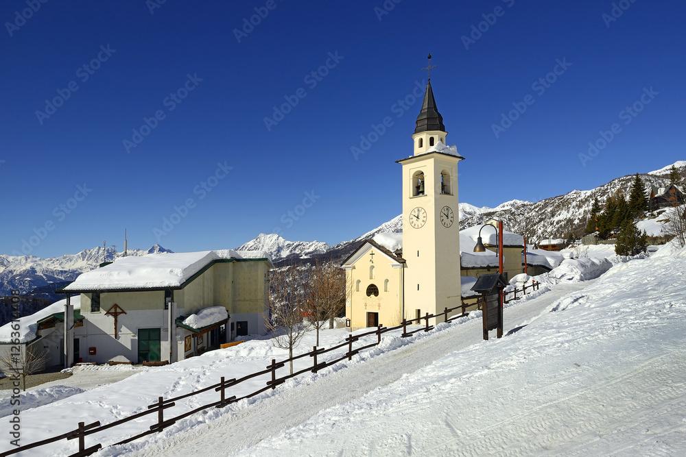 Church in the center of the village in winter. The village lies in the valley leading to the Breuil-Cervinia below the mountain Matterhorn peak - Monte Cervino, Chamois, Italy