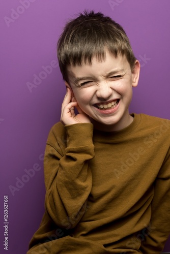 A young boy in distress holding his ear, suffering from earache. Useful for medical content, hearing health, otitis, and seasonal illness awareness campaigns.