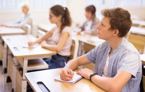 Portrait of focused teenage student writing lectures in workbooks in classroom during lesson.. photo