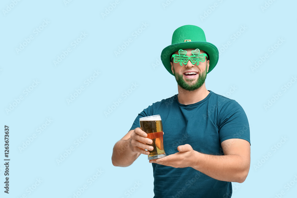 Young man in leprechaun hat and decorative glasses in shape of clover with green beard holding glass of beer on blue background. St. Patrick's Day celebration Young man in leprechaun hat and decorative glasses in shape of clover with green beard holding glass of beer on blue background. St. Patrick's Day celebration