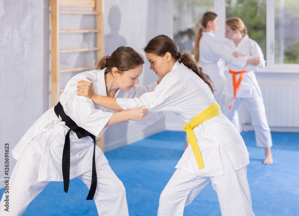 Obraz premium Pairs classes in judo or jiu-jitsu - two teenage girls practice grabbing and throwing on sports mats