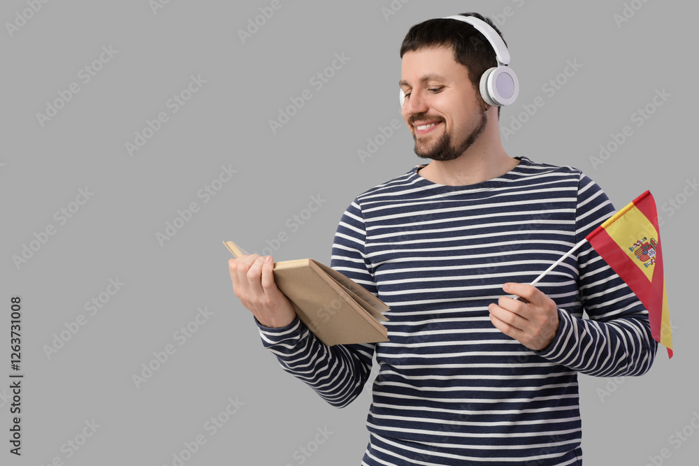 Handsome man in headphones with flag of Spain and book on light background Handsome man in headphones with flag of Spain and book on light background