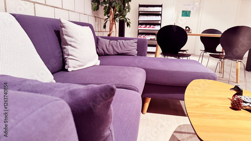 Cozy office lounge with purple sectional sofa, white cushions, wooden coffee table with duck figurine and pine cone, black chairs, and bookshelf in background. High quality photo photo