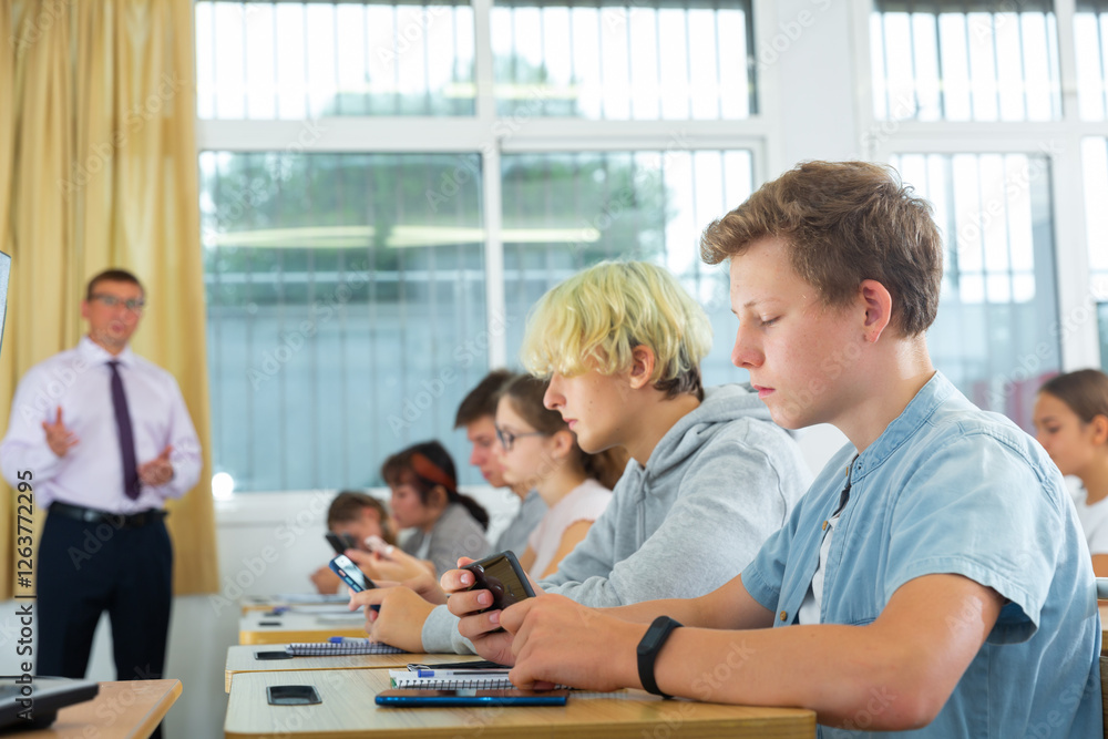 Group of focused teenagers using phones at class in auditorium Group of focused teenagers using phones at class in auditorium