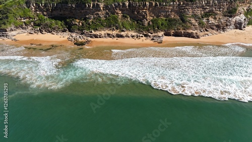 Drone shot aerial view of a headland and waves crashing at the base of a cliff in summer in Australia 