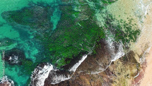 Drone shot aerial view of a reef and waves crashing onto rocks near a beach in Australia in summer 