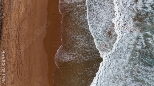 Drone shot aerial view of a beach and waves crashing onto the shore 