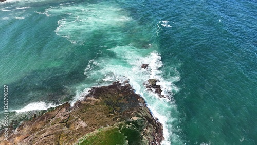 Drone shot aerial view of waves crashing onto rocks on a reef near a beach in Australia 