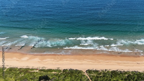 Drone shot aerial view of waves crashing onto the beach in summer in Australia