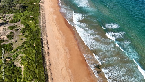 Drone shot aerial view of a beach and waves crashing onto the shore in summer in Australia 
