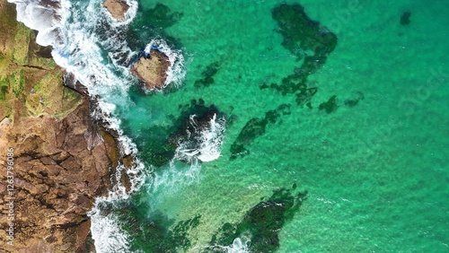 Drone shot aerial view of a reef and clear blue water and waves crashing onto rocks 