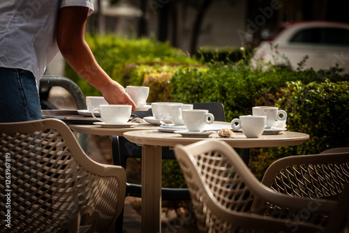 A bar terrace table scattered with empty coffee cups is swiftly cleared by a waiter in valencia, spain, reflecting the region’s café culture and hospitality routine in everyday city life. photo