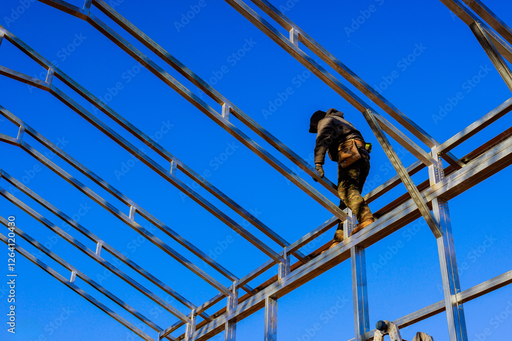 Worker balances carefully on steel beams while constructing commercial building framework Worker balances carefully on steel beams while constructing commercial building framework