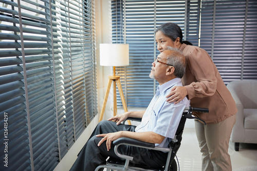 Bild auf Leinwand senior woman standing beside senior man sitting on wheelchair and looking outsid