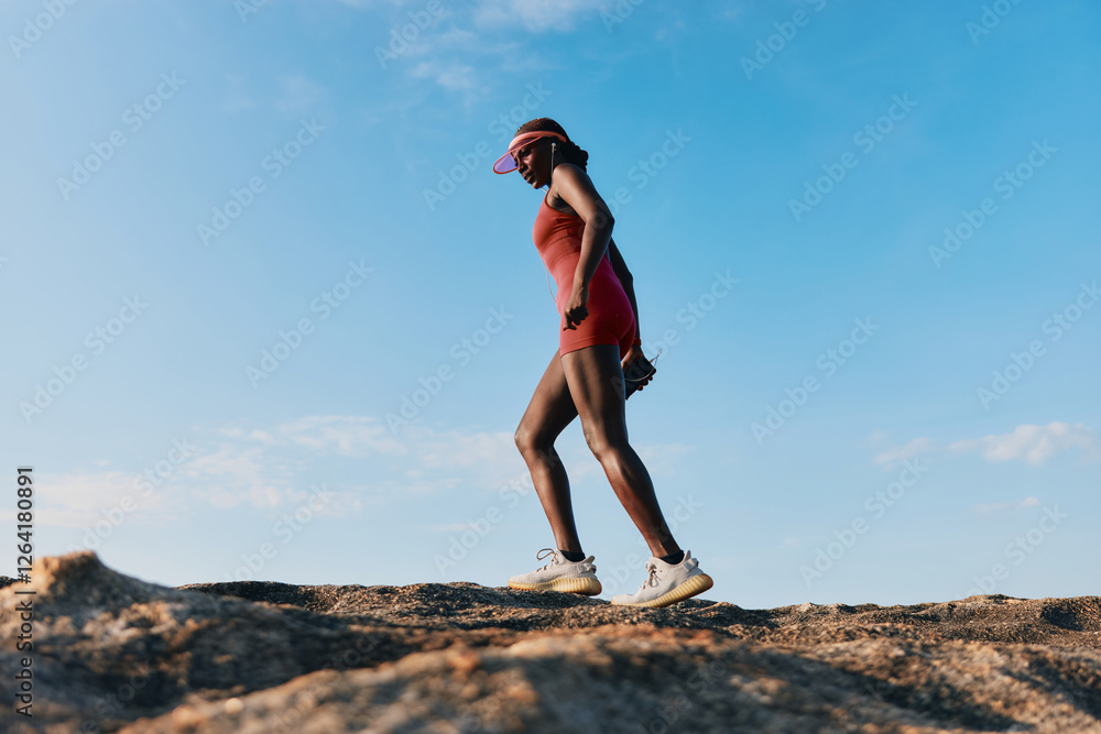 Woman hiking on rocky terrain under a clear blue sky, wearing athletic clothes and a visor, showcasing an active lifestyle Woman hiking on rocky terrain under a clear blue sky, wearing athletic clothes and a visor, showcasing an active lifestyle