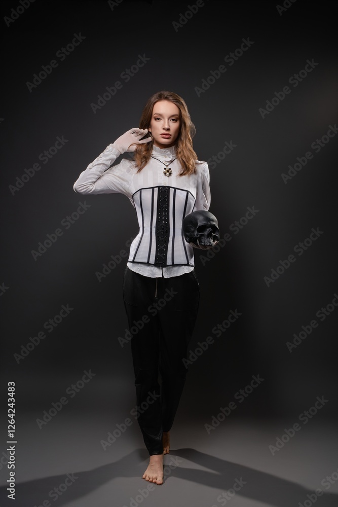 Elegant woman in corset holding skull gazes confidently in dark studio Elegant woman in corset holding skull gazes confidently in dark studio
