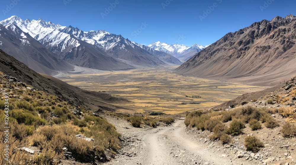 Scenic mountain valley with winding dirt road, surrounded by towering peaks and clear blue sky