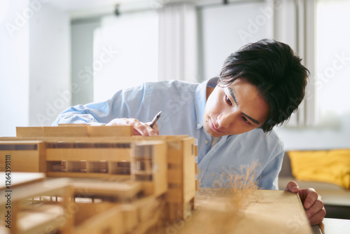 事務所で建築の模型を見ながら設計士として働く1人の30代の男性