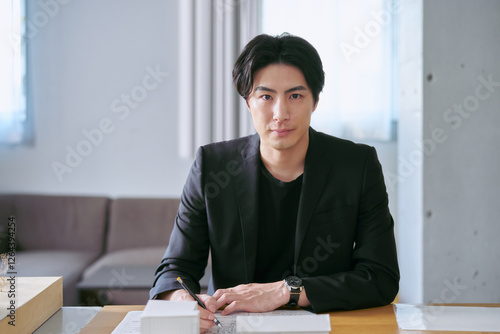 建物の模型を前に設計図を書きながら建築を設計するカメラ目線の建築士の男性