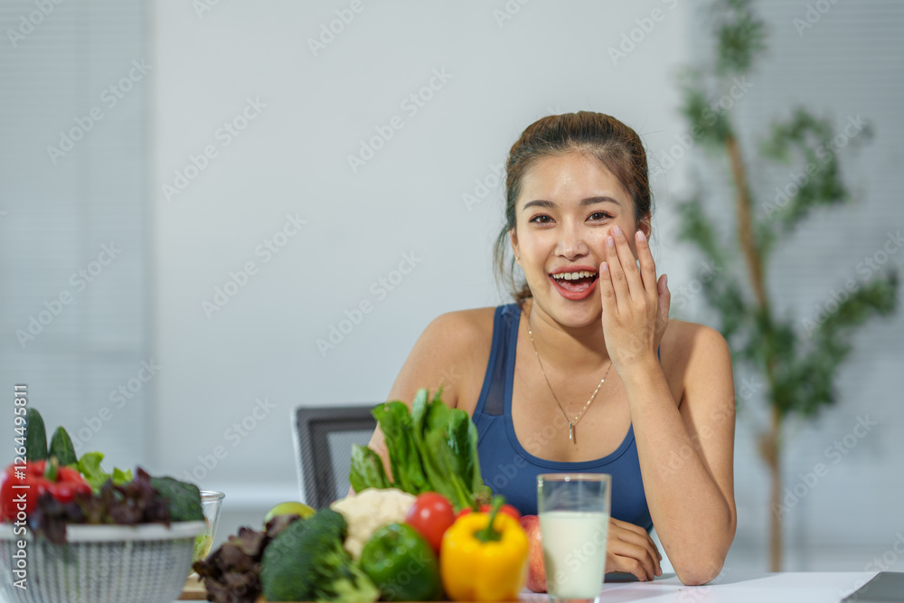 Asian woman wearing sportswear is sitting at a table with a glass of milk and a variety of fresh vegetables. Touching her face with a happy and surprised expression. Promoting a healthy lifestyle Asian woman wearing sportswear is sitting at a table with a glass of milk and a variety of fresh vegetables. Touching her face with a happy and surprised expression. Promoting a healthy lifestyle