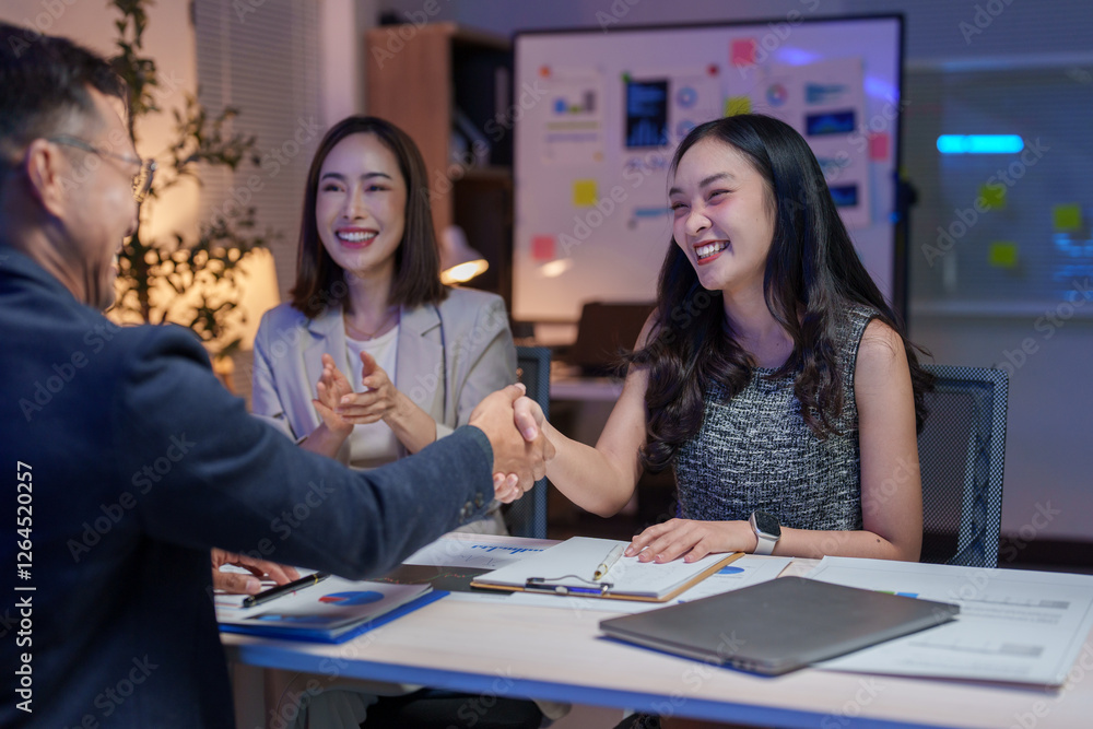 Asian businesspeople shaking hands over a desk in a brightly lit office at night, celebrating the successful conclusion of a meeting with smiles and positive energy Asian businesspeople shaking hands over a desk in a brightly lit office at night, celebrating the successful conclusion of a meeting with smiles and positive energy