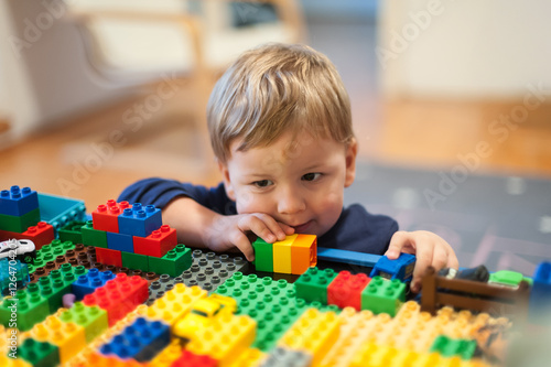 A young child focuses intently on constructing with vibrant building blocks. The playful environment is filled with various colors and shapes, promoting imagination and creativity.