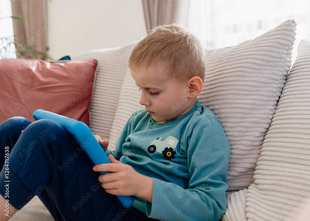 a 4-year-old boy sits on the sofa at home with a tablet. High quality photo a 4-year-old boy sits on the sofa at home with a tablet. High quality photo