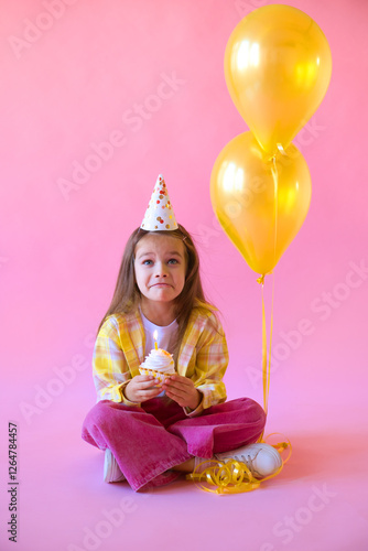 unhappy little girl in party cap for her birthday makes wish and blows out candle on cake.