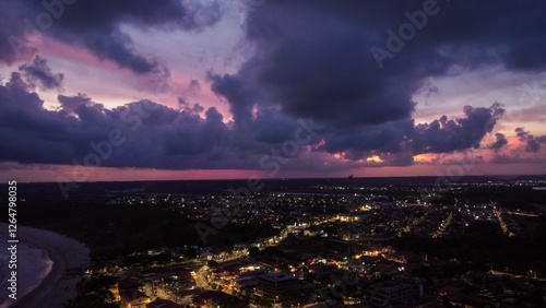 Aerial view of coastal city at dusk with dramatic clouds.