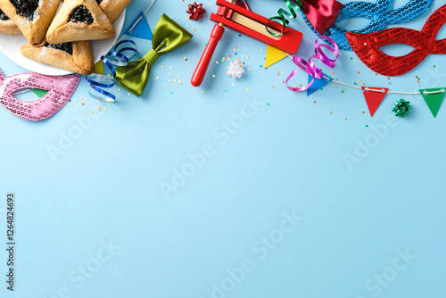 Purim celebration concept. Flat lay composition with hamantaschen cookies, masks, noisemaker, and festive decorations on a blue background. photo